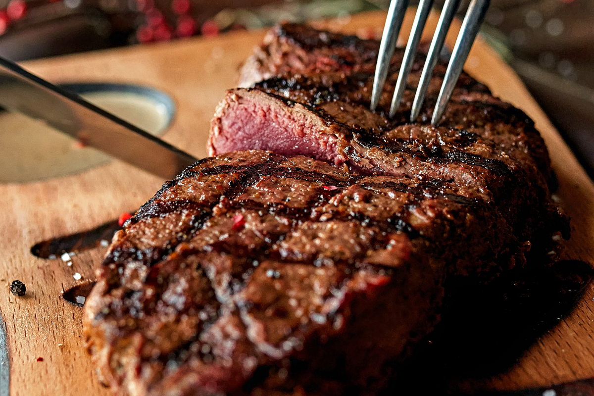 A close-up view of a grilled steak being sliced on a wooden cutting board.