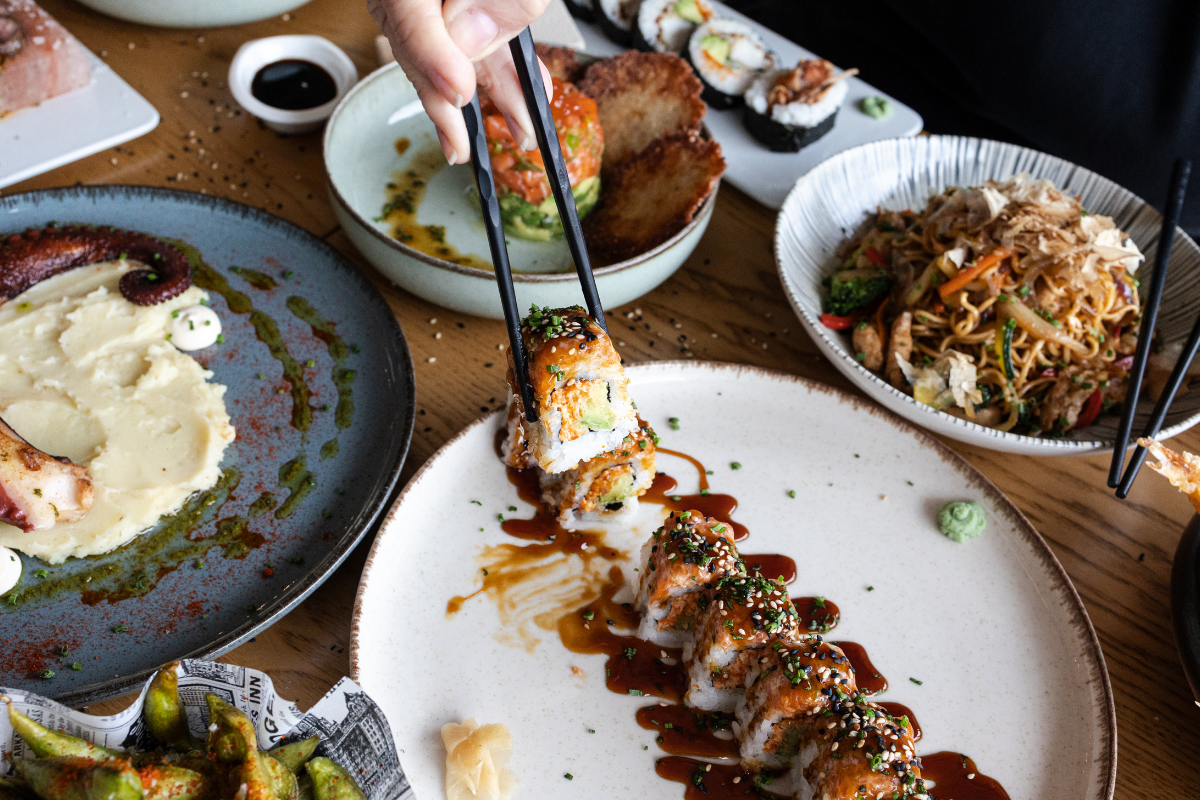 A variety of Asian dishes including sushi rolls, octopus, and noodles displayed on a wooden table.