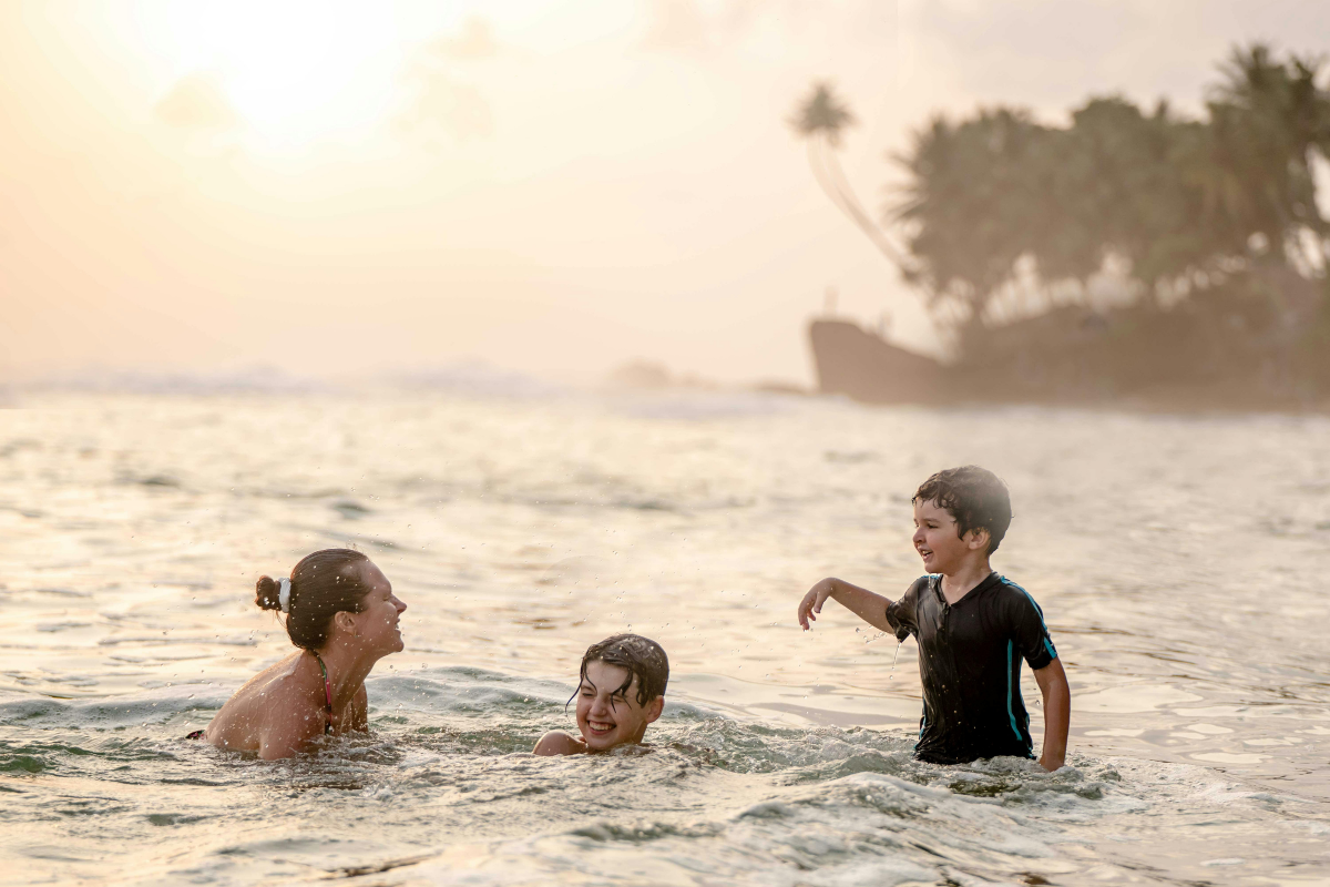 Mother and two children laughing and playing in the warm ocean waves at sunset